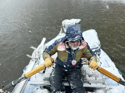 Man with icicles in beard rowing a boat on a river